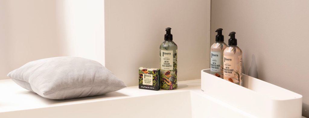Itinera dispensers on a bedroom shelf beside a linen pillow